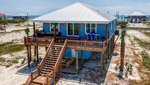 A beachfront house with a deck, outdoor seating, and a staircase leading to the entrance.
