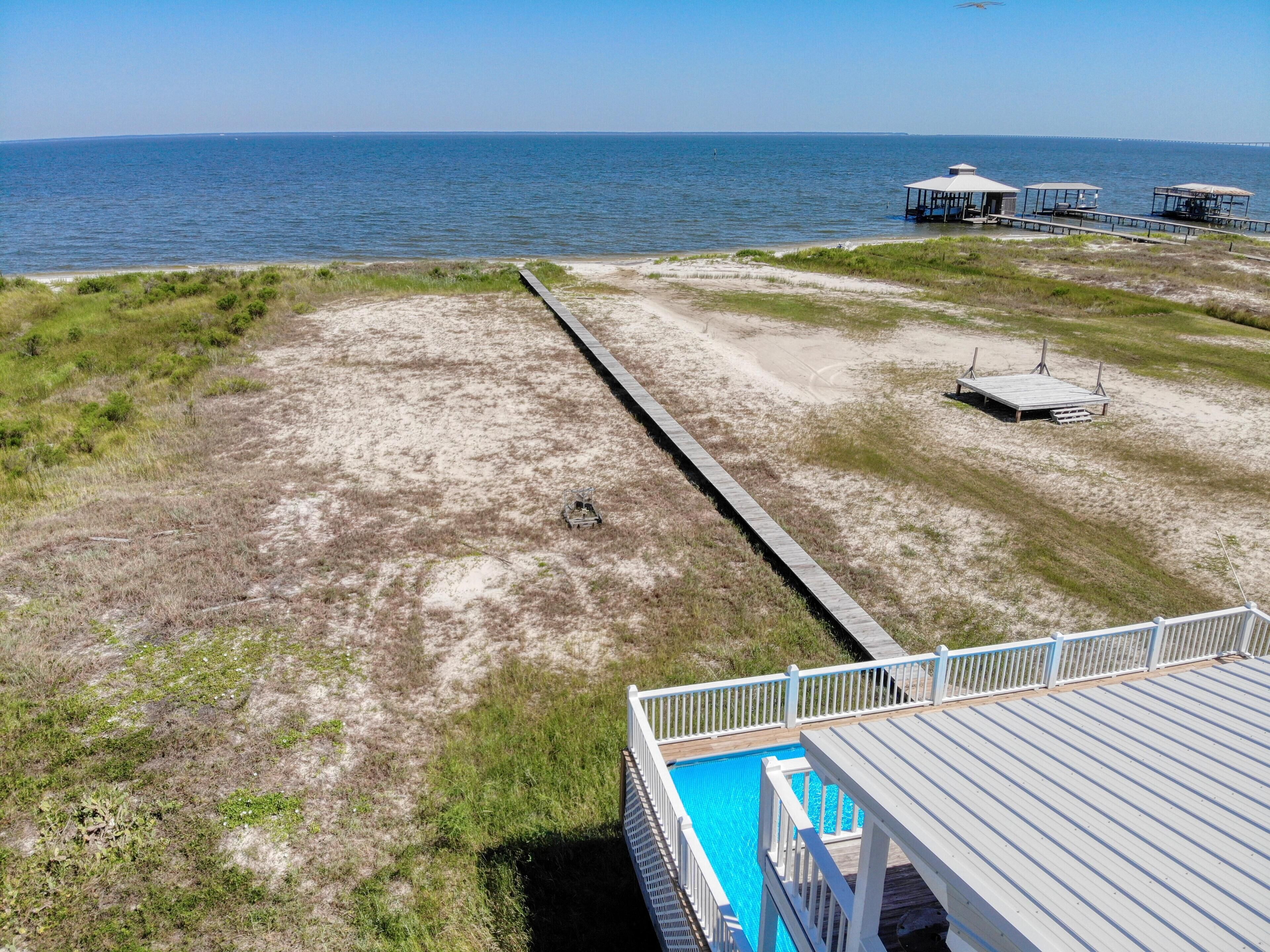 A beach with a wooden walkway leading to a pool area, a pier with structures, and a clear view of the ocean.