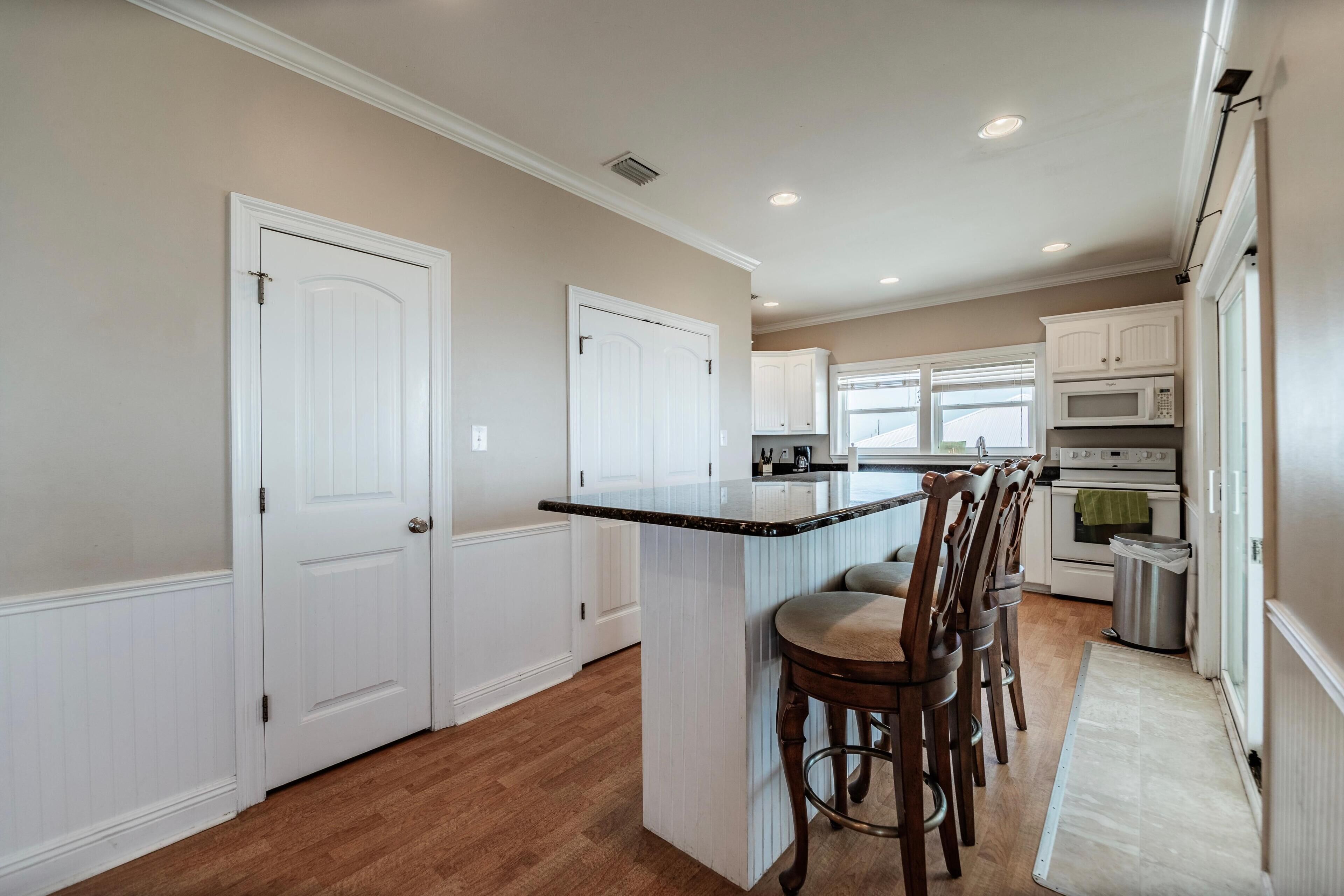 A kitchen with a central island, white cabinetry, and a stainless steel trash can.