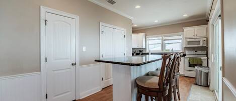 A kitchen with a central island, white cabinetry, and a stainless steel trash can.