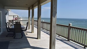 A covered outdoor deck with a wooden railing overlooking the ocean.