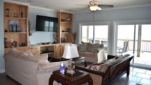 Un salón amplio con una televisión de pantalla plana grande, estanterías de madera y un balcón con mobiliario exterior.