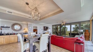 A spacious living area with a dining table, red sofa, and large windows offering a view of palm trees. - Holiday Isle #122 (Dauphin Island)