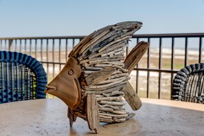 A decorative fish sculpture made of driftwood on a table with a view of the beach in the background.