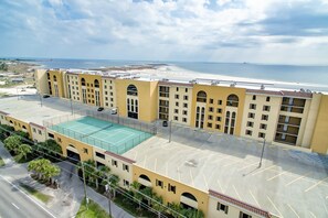 A multi-story hotel with a rooftop tennis court, a parking lot, and a view of the beach and ocean.