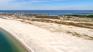 Ett flygbildsbild av ett kustområde med en sandstrand, en stor byggnad och en bro i fjärran.