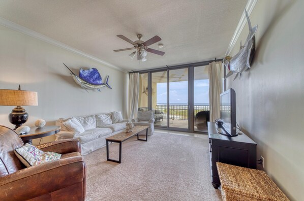 A living room with a ceiling fan, a large window with curtains, a television, and a fireplace.
