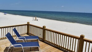 Eine Holzterrasse mit blauen Liegestühlen mit Blick auf einen Strand.