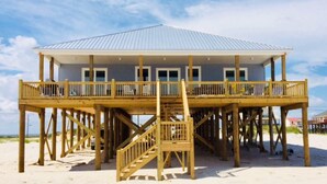 Ein Strandhaus mit einer Holzdielen-Terrasse, einer überdachten Veranda und einer Treppe zum Hauptgeschoss.
