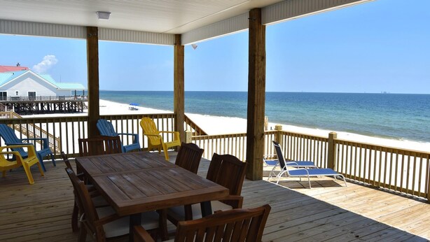 Eine Holzterrasse mit Tisch und Stühlen, mit Blick auf Strand und Meer.