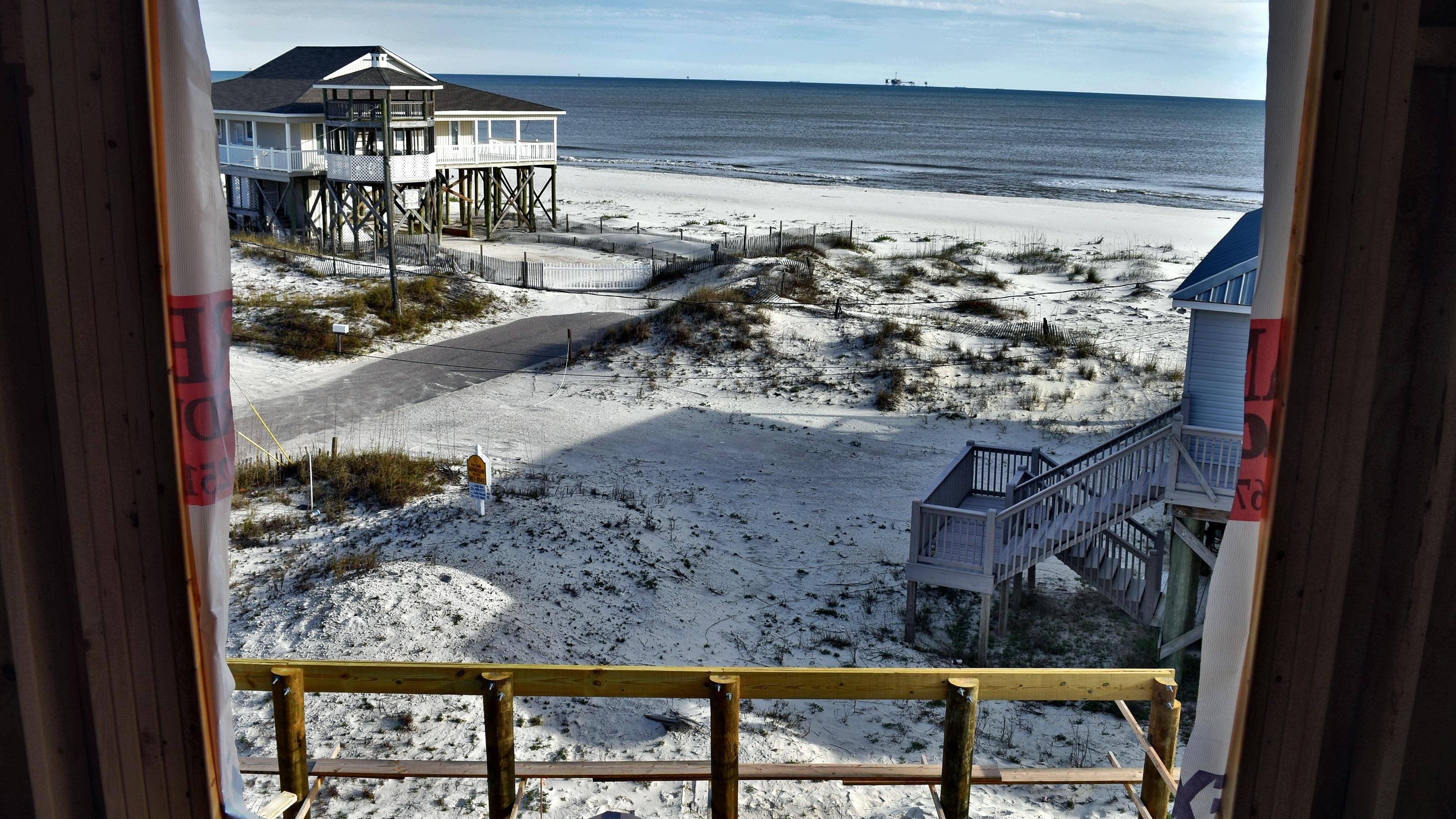 A beach view from a wooden deck with a view of the ocean, a sandy beach, and a building with a balcony.