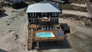 A two-story beach house with a pool on the second level, deck chairs, and a covered patio. - Sonny Daze - 105 Quebec Ct (Dauphin Island)