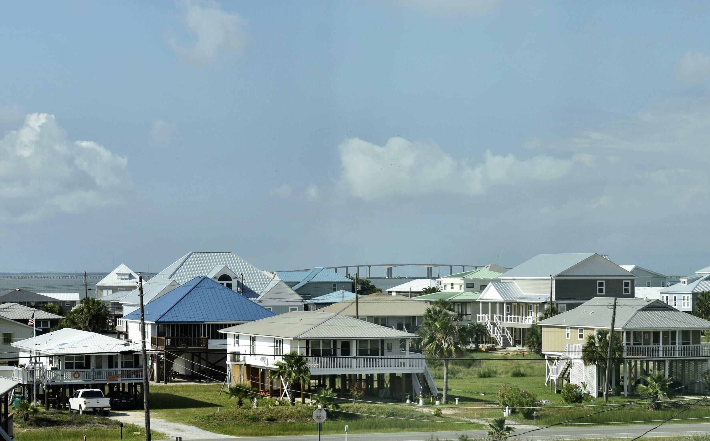 A coastal residential area with houses featuring various roof styles and a prominent bridge in the background.