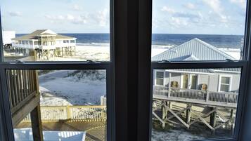 Vista de una casa de playa con terraza de madera y balcón con vista al océano.