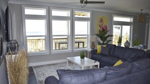 A living room with a grey sofa, white coffee table, and large windows with a view of the outside. - Sonny Daze - 105 Quebec Ct (Dauphin Island)