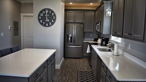 A modern kitchen with a stainless steel refrigerator, a built-in oven, and a large wall clock. - Sonny Daze - 105 Quebec Ct (Dauphin Island)