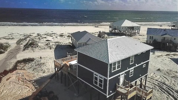 A beachfront house with a metal roof, multiple decks, and a sandy beach in the background. - Sonny Daze - 105 Quebec Ct (Dauphin Island)