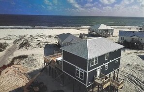 Uma casa à beira-mar com telhado de metal, várias varandas e uma praia arenosa ao fundo.