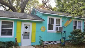 A turquoise house with a white door, yellow shutters, and a sun decoration on the wall. - Surf Shack - 1013 Cadillac (Dauphin Island)
