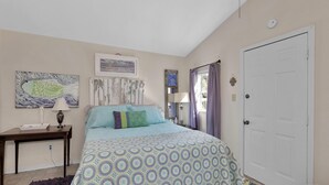 A bedroom with a bed, a nightstand, a desk, and a door. - Surf Shack - 1013 Cadillac (Dauphin Island)