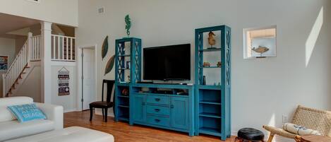 A living room with a white sofa, a teal entertainment unit, a flat-screen TV, and a wicker chair.