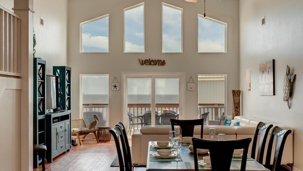 Un comedor con una mesa dispuesta para cuatro personas, un sofá y vistas al exterior a través de amplios ventanales.