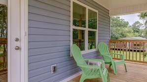 Un porche techado con dos sillas Adirondack verdes, una ventana con persianas y una terraza de madera.