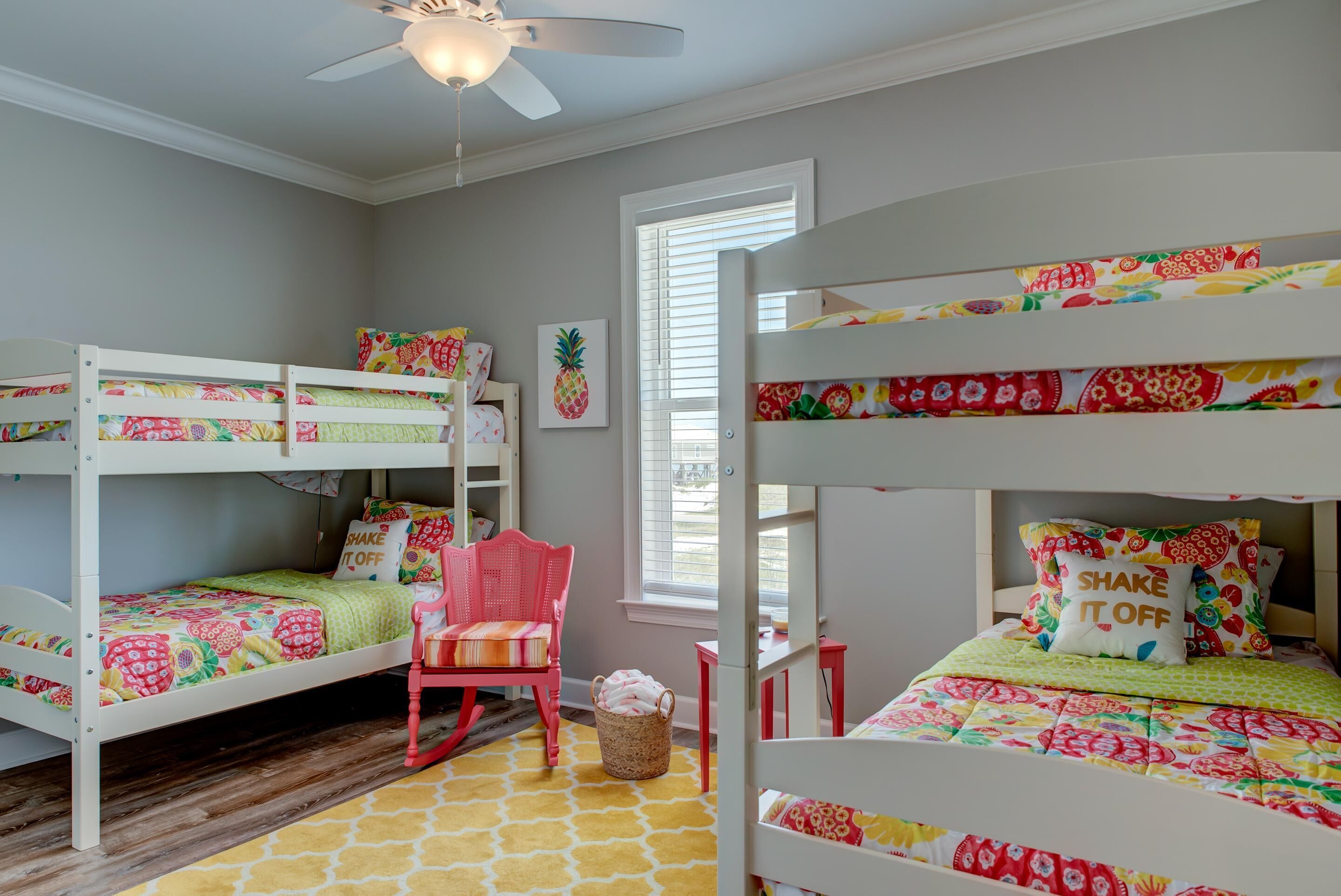 A child's bedroom with bunk beds, a ceiling fan, a window with blinds, and a chair.