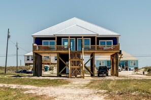 A two-story beach house with a balcony, a wooden deck, and a metal roof. - Blue Oasis - 2500 Bienville Blvd (Dauphin Island)