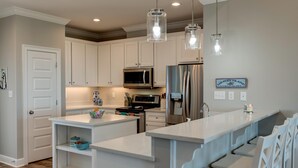 Una cocina moderna con armarios blancos, electrodomésticos de acero inoxidable e iluminación colgante.