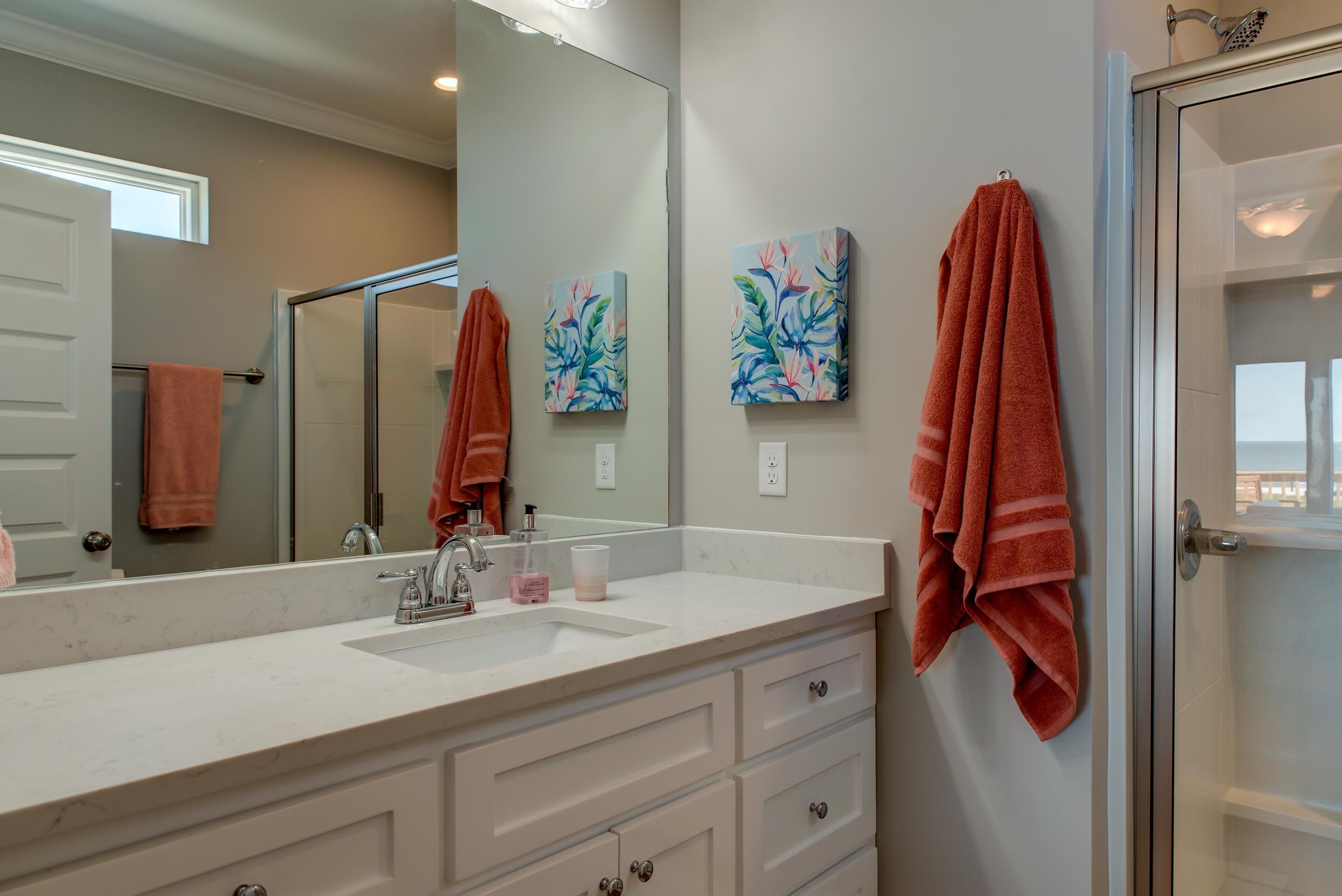 A bathroom with a white sink, a large mirror, and two wall-mounted paintings.