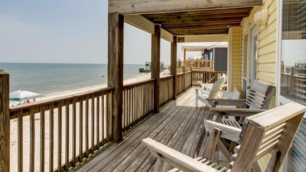 A wooden deck with a view of the ocean, outdoor seating, and a covered area with a view of the beach.