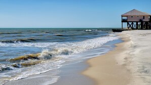 A beach with a wooden pier and a building on stilts.