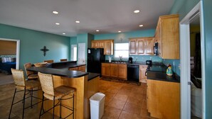 A spacious kitchen with wooden cabinets, a black refrigerator, and a dining area with wicker chairs. - Sun Spot - 104 Vargas Ct (Dauphin Island)