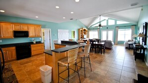 A spacious kitchen with wooden cabinets, a microwave, and a large island with bar stools. - Sun Spot - 104 Vargas Ct (Dauphin Island)