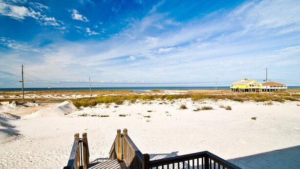 A beach with a wooden boardwalk leading to a yellow building with a beachside view. - Sun Spot - 104 Vargas Ct (Dauphin Island)