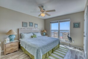 Een slaapkamer met een groot bed, een plafondventilator, een raam met uitzicht en een decoratief vogelbeeldje.