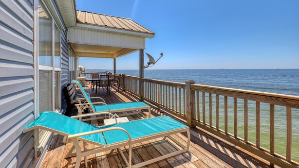 A wooden deck with lounge chairs and a covered area overlooking the ocean.