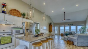 A spacious kitchen with a large island, bar stools, and a view of the ocean through large windows.