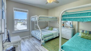 A bunk bed room with a ceiling fan, a window with a view, a desk with a computer, and a dresser.