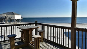 Una terraza de madera con una mesa y taburetes con vistas a la playa.