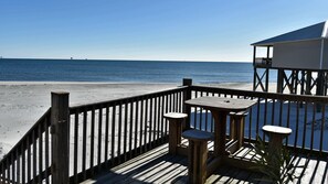 Um deck de madeira com uma mesa e bancos, com vista para uma praia e o oceano.