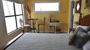Quarto com uma cama grande, janela, uma mesinha com abajur, cadeira e um vaso decorativo.
