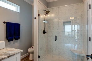 A bathroom with a glass-enclosed shower, a marble countertop, and a toilet. - Serenity Now - 2442 Bienville (Dauphin Island)