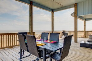 A covered outdoor deck with a table and chairs, overlooking a beach. - Serenity Now - 2442 Bienville (Dauphin Island)