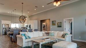A spacious living room with a white sofa, a coffee table, and a dining area with chairs. - Serenity Now - 2442 Bienville (Dauphin Island)