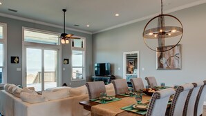 A modern living room with a dining area, featuring a sofa set, a wooden dining table, and a large chandelier. - Serenity Now - 2442 Bienville (Dauphin Island)