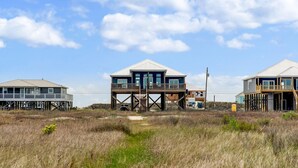 A beachfront house with a deck and a staircase leading to the main floor. - Serenity Now - 2442 Bienville (Dauphin Island)