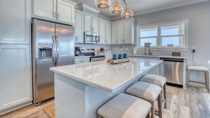 A modern kitchen with white cabinets, stainless steel appliances, a large island with bar stools, and a pendant light fixture. - Endless Possibilities-1809 Bie (Dauphin Island)