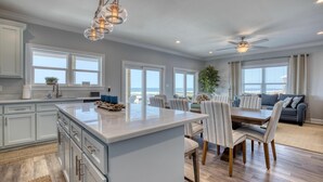 A spacious kitchen with a large island, dining area with striped chairs, and a ceiling fan. - Endless Possibilities-1809 Bie (Dauphin Island)